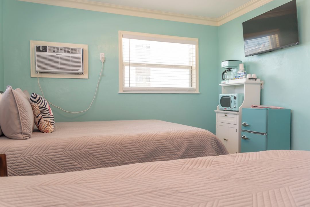 Ein Zimmer mit zwei Betten, einem Fenster, einer Klimaanlage, einer Mikrowelle und einem Fernseher an der Wand.