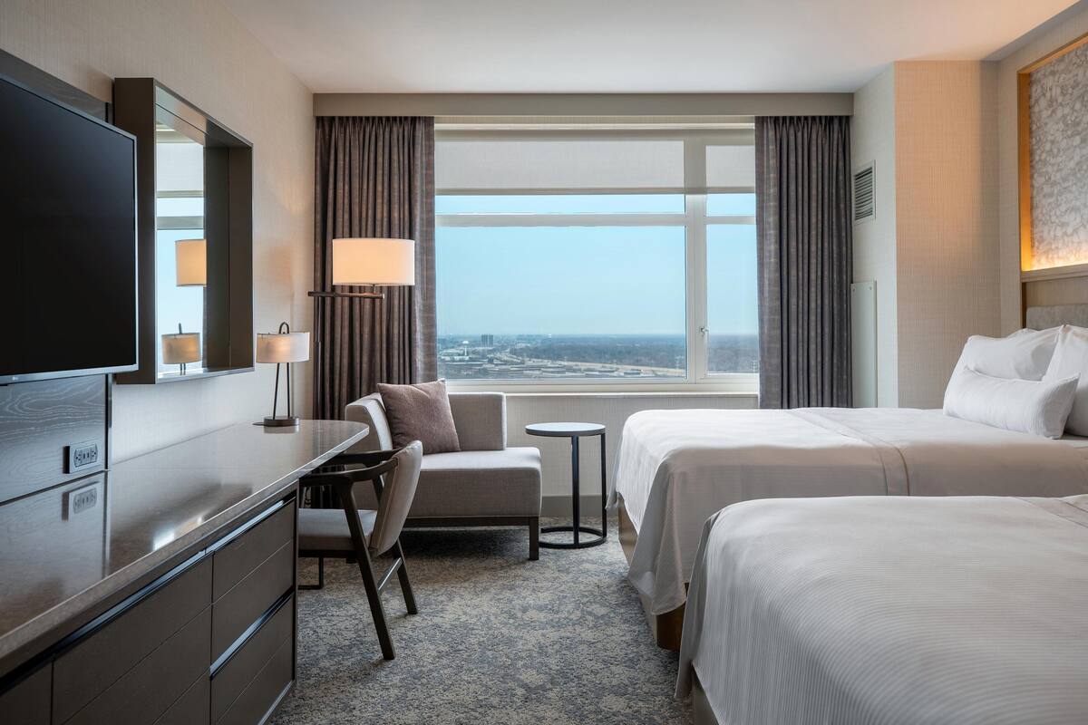 A hotel room with a bed, a desk, a chair, a TV, and a window with a city view.