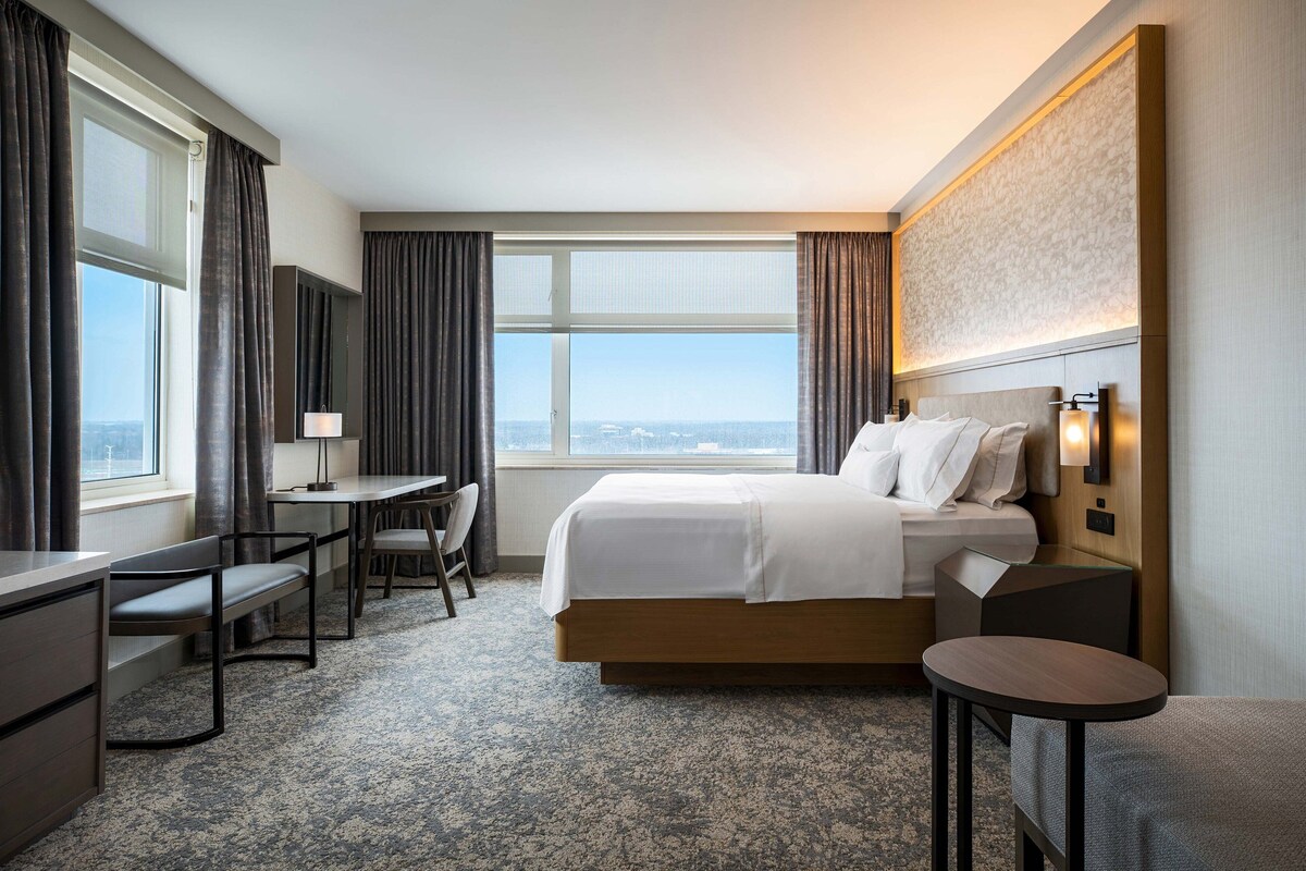 A hotel room with a large bed, a desk, a chair, and a small table.