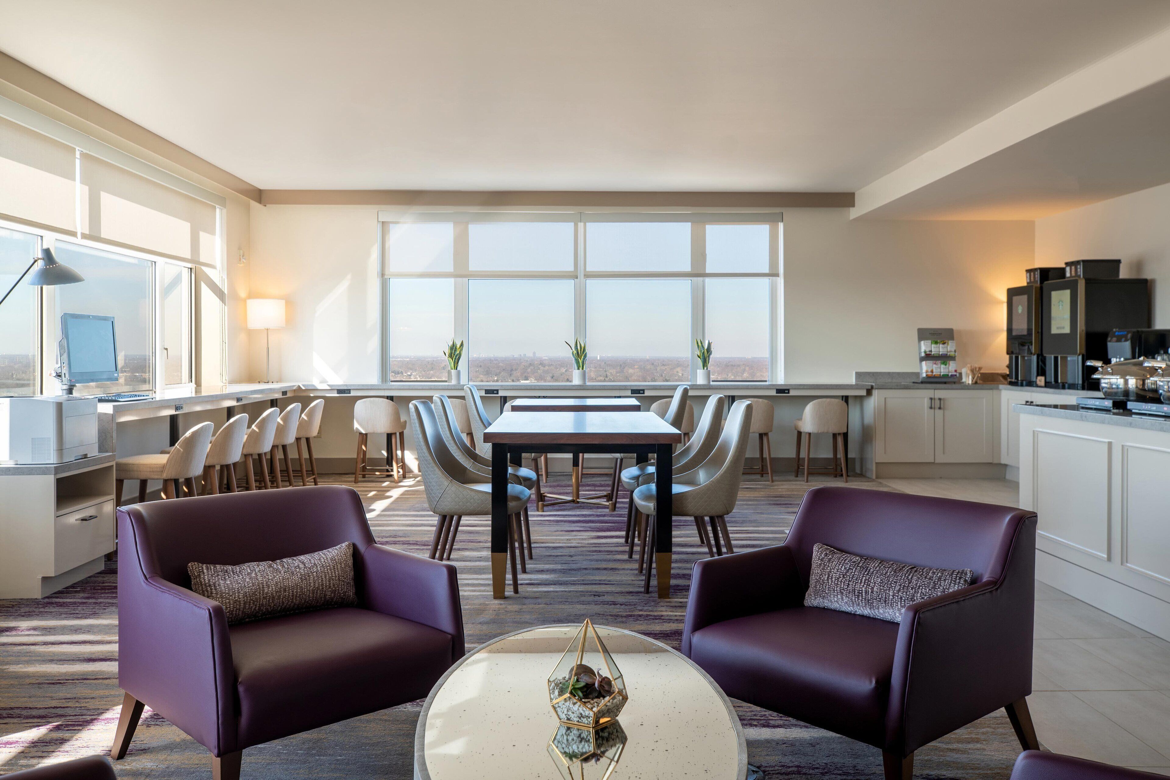 A modern hotel room with a dining area, a kitchen, and a view of the city.