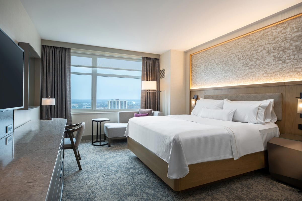 A modern hotel room with a large bed, a desk, a chair, and a TV.