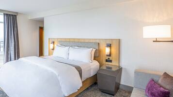Habitación de hotel con una cama grande, mesitas de noche, un sofá y una ventana con cortinas.