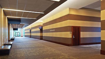 Un couloir avec un tapis à motifs, une porte en bois portant l’inscription « Salle de bal pour les jeunes », et une rangée de bancs le long du mur gauche.