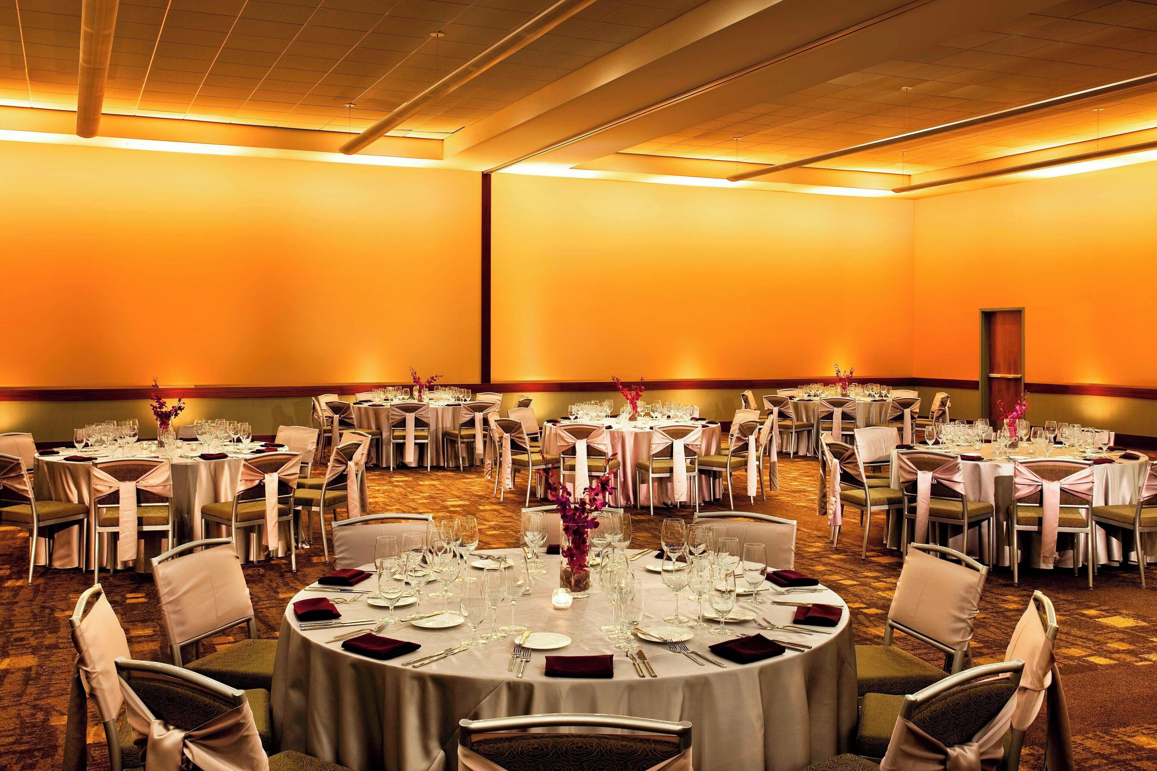 Un salón de banquetes con mesas redondas dispuestas para comer, con manteles blancos y cubertería ordenada.