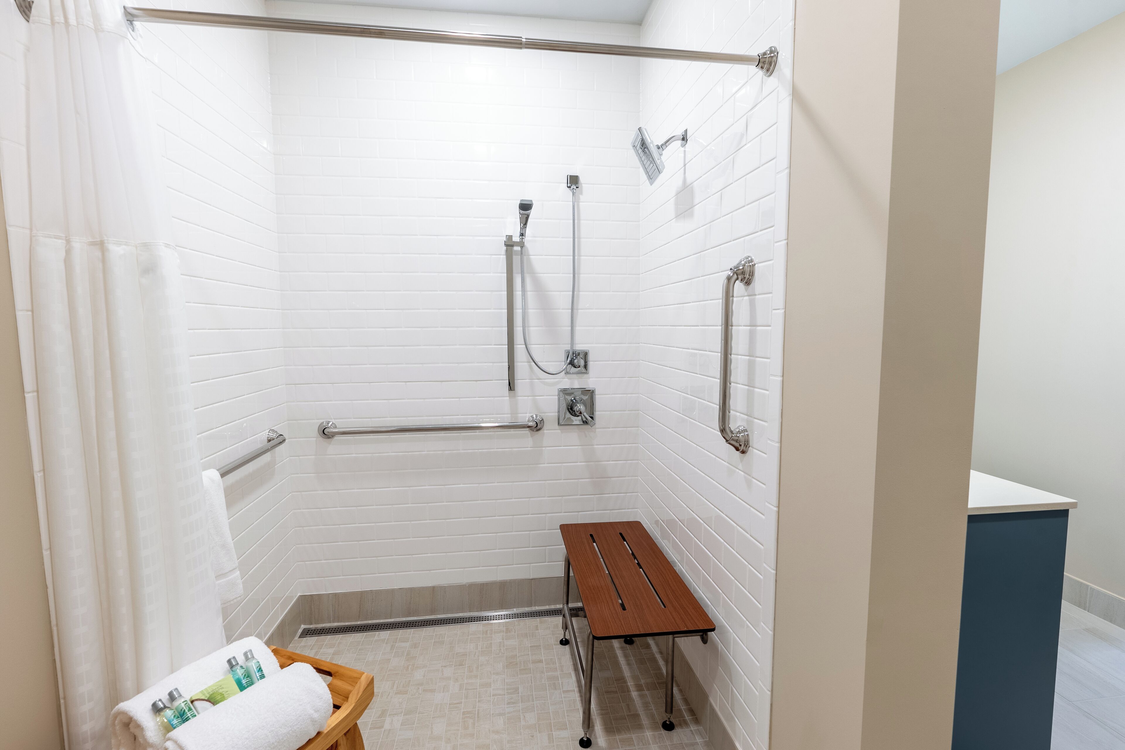 A wheelchair-accessible shower area with grab bars, a bench, and a towel rack.