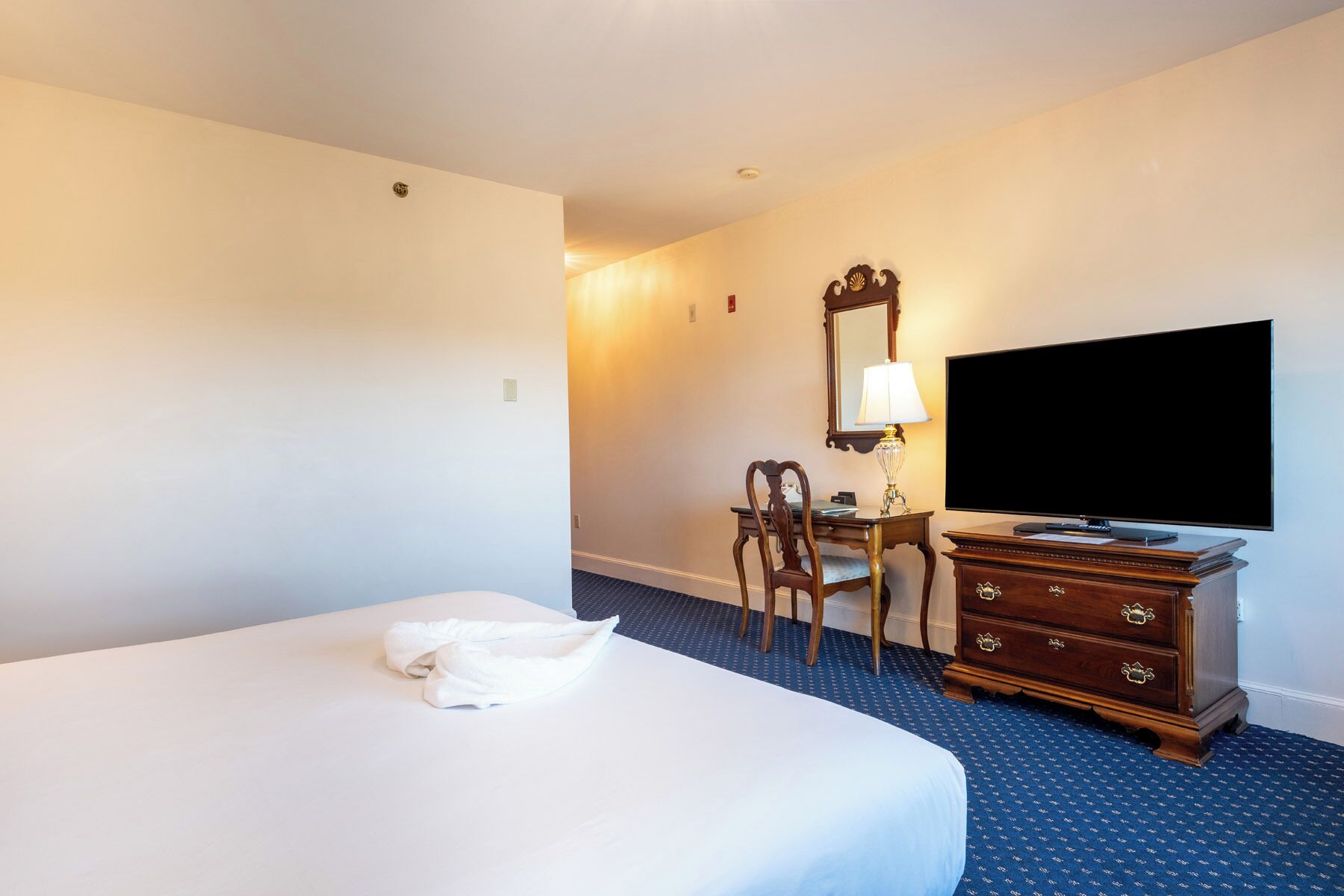 A hotel room with a bed, a desk with a chair, a dresser, and a TV.