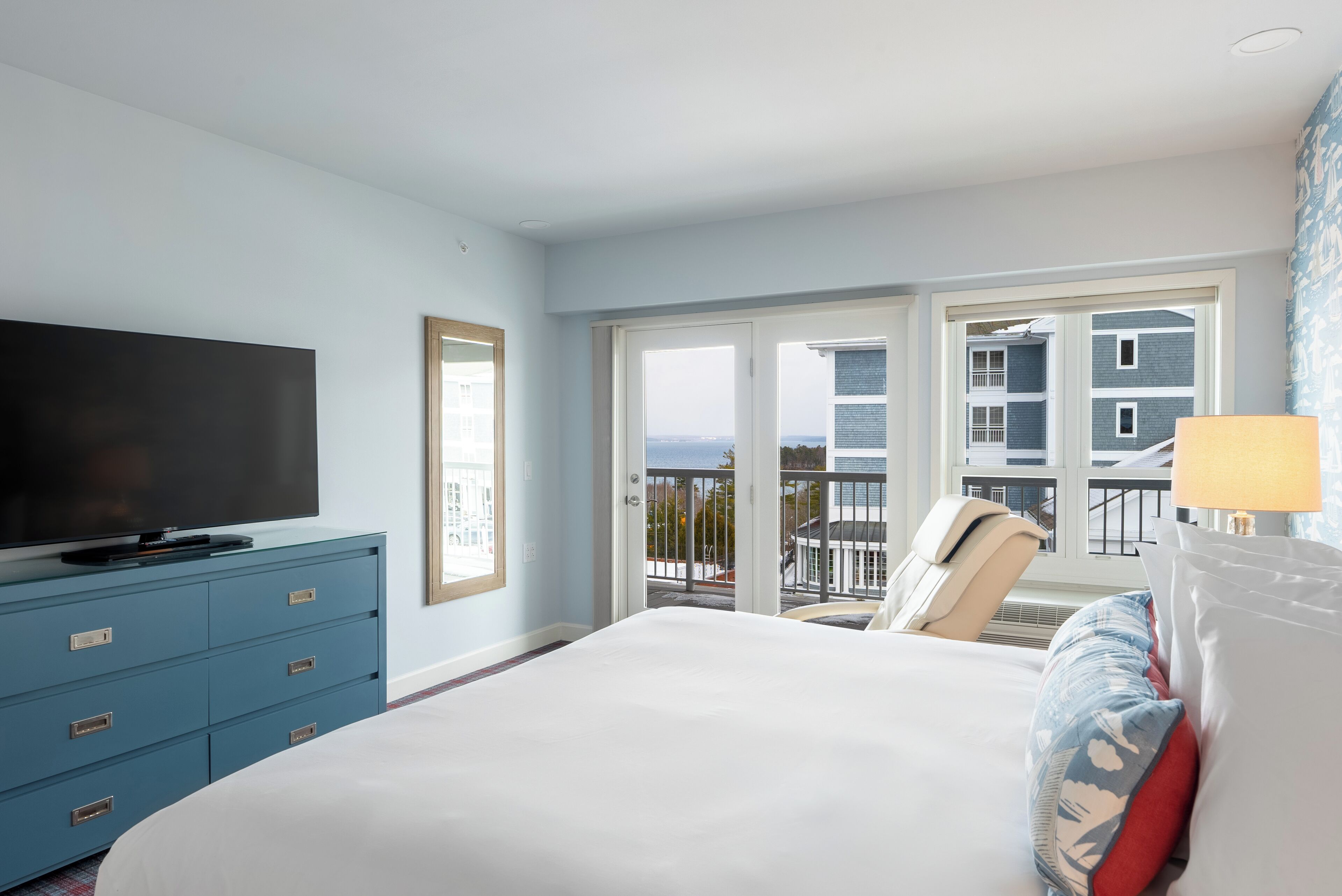 A hotel room with a bed, a television on a dresser, a balcony with a view of buildings and the sea.