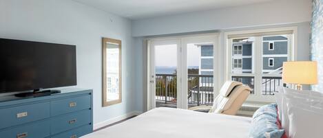 A hotel room with a bed, a television on a dresser, a balcony with a view of buildings and the sea.