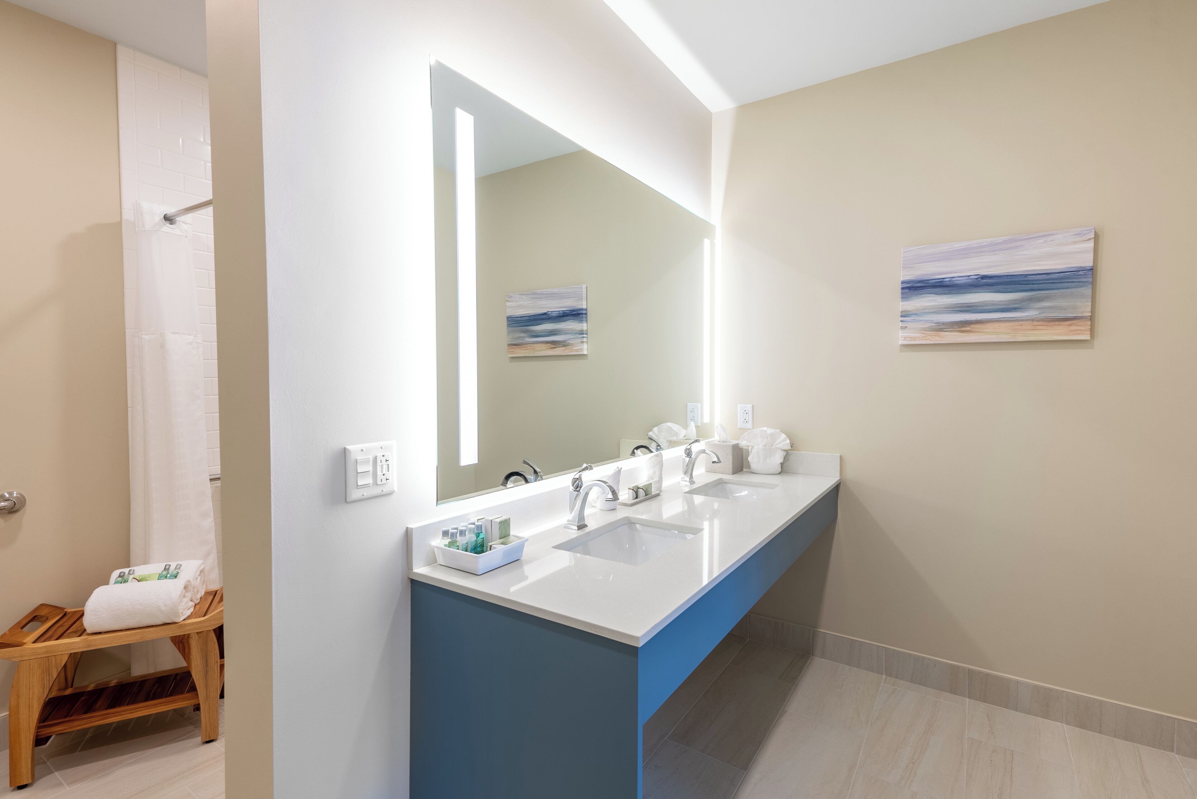 Une salle de bain moderne avec deux lavabos, un grand miroir et un banc en bois.