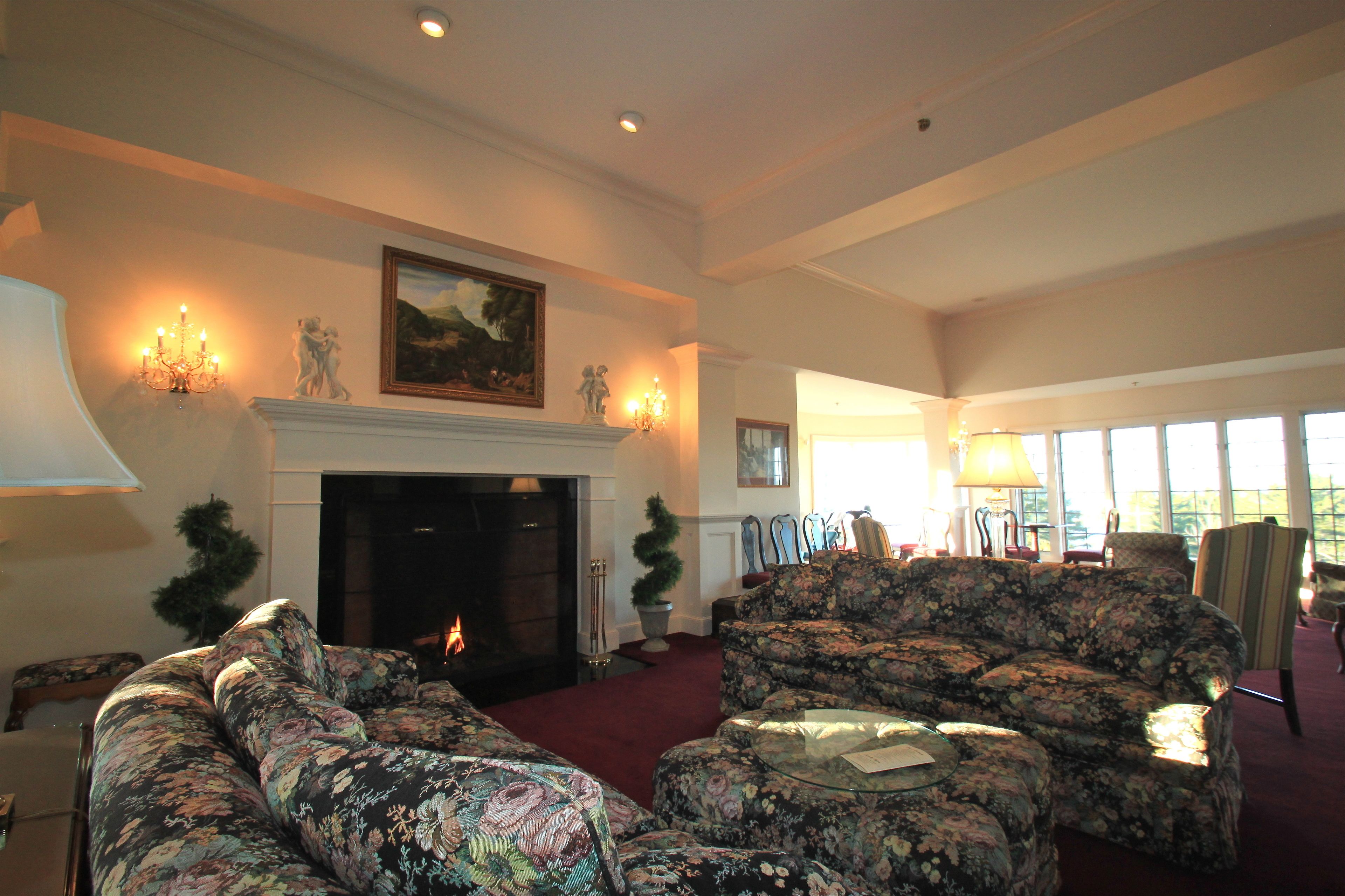 A spacious living room with a fireplace, floral upholstery, and a large window providing natural light.