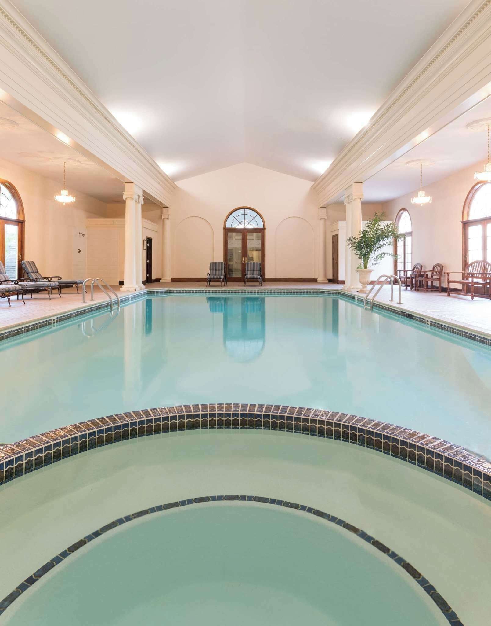 Ein großer, überdachter Schwimmteich mit Fliesenbord, umgeben von Liegestühlen und einem Blumentopf.