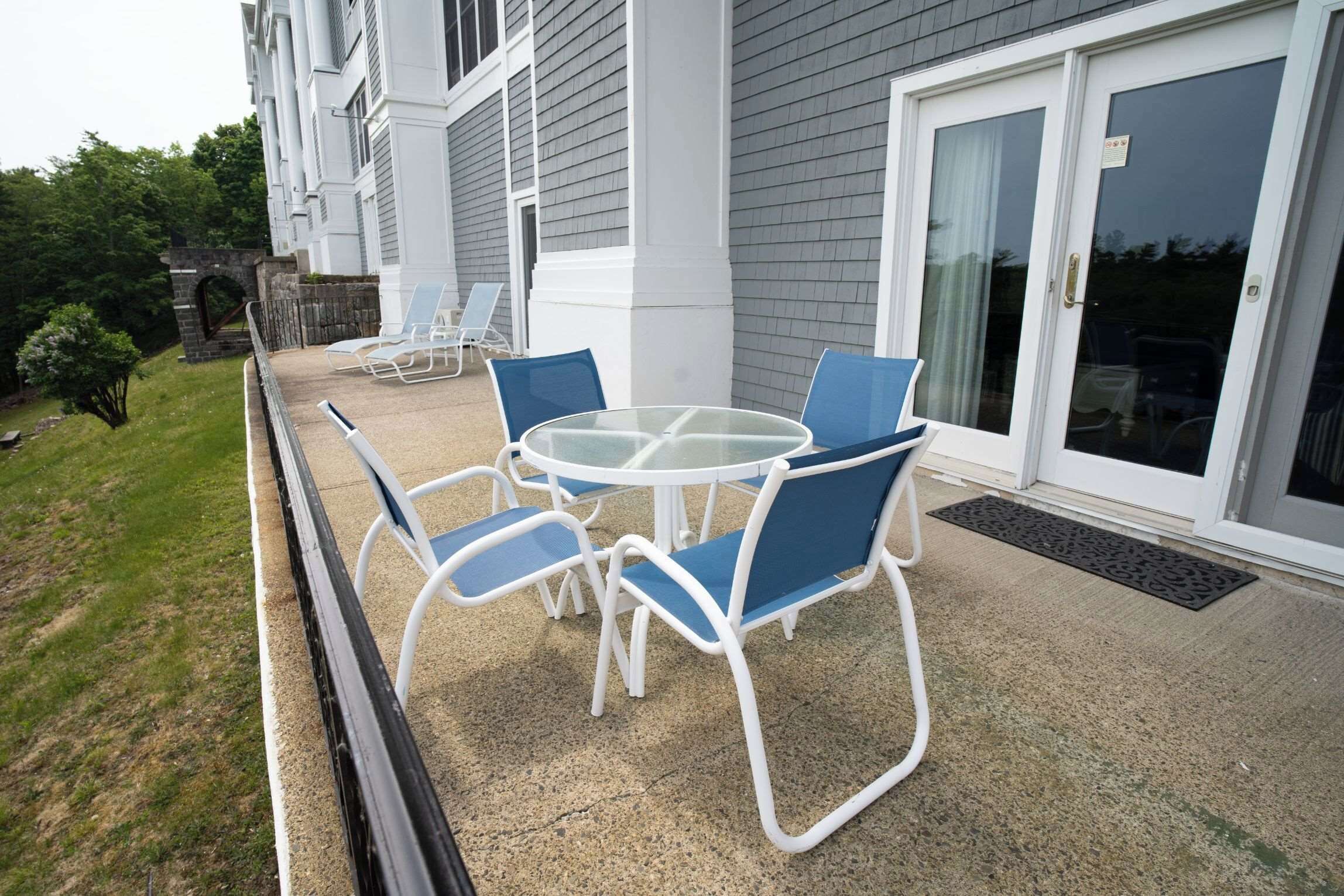 A patio with a round table and four chairs, a stone archway, and a building with a grey exterior and white trim.
