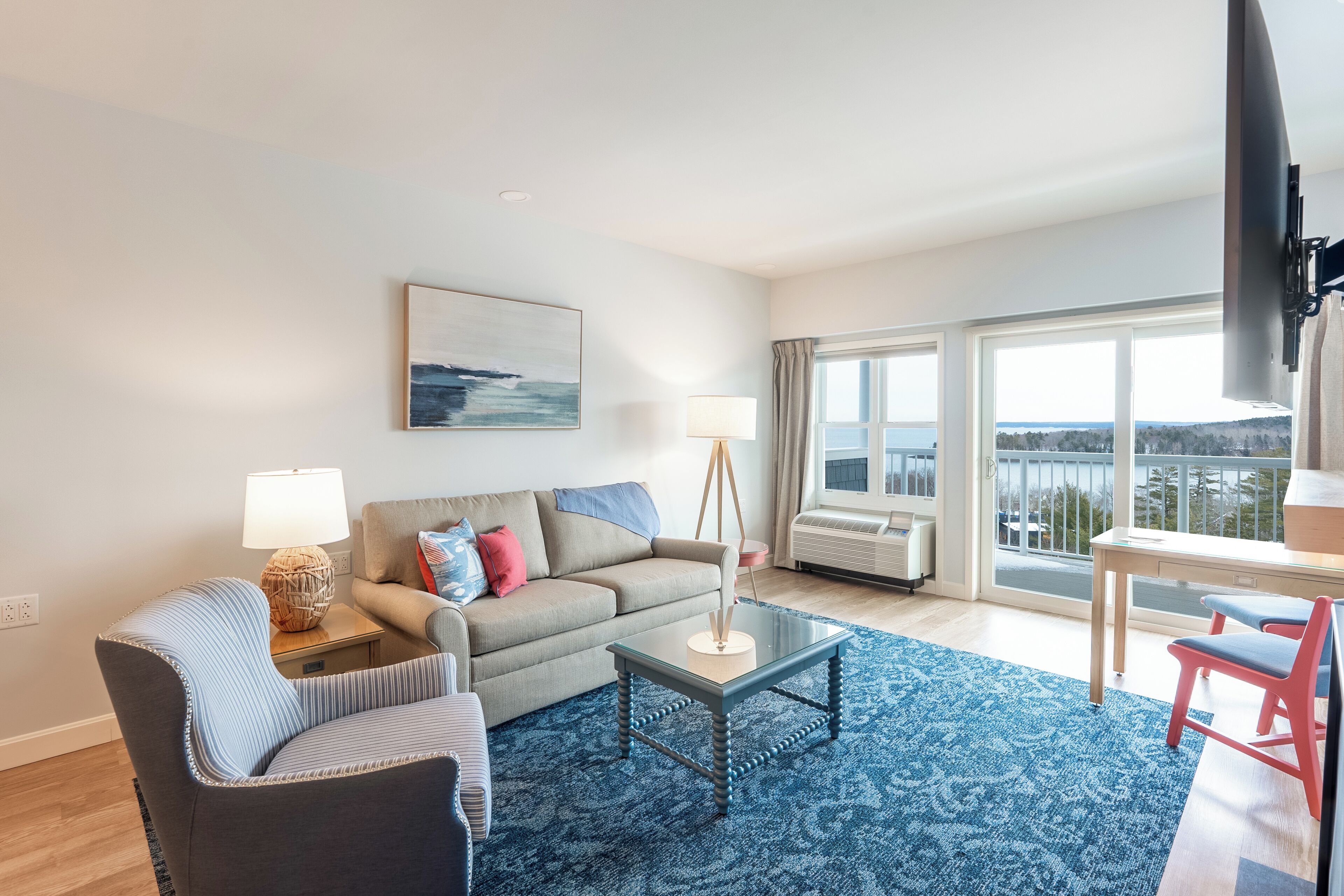 Una sala moderna con sofá, sillón, mesa de centro y vistas al exterior a través de amplios ventanales.