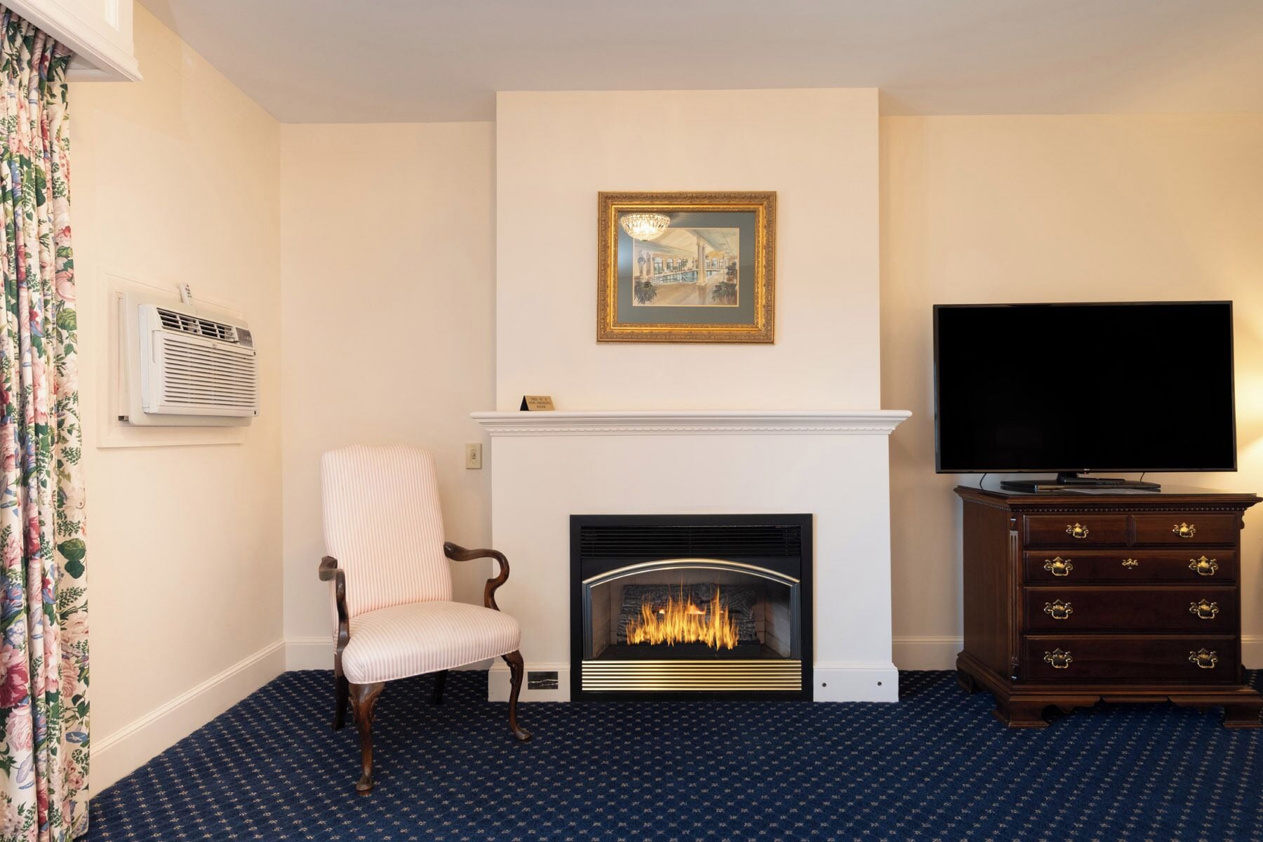 A room with a fireplace, a television, a chair, and a patterned carpet.