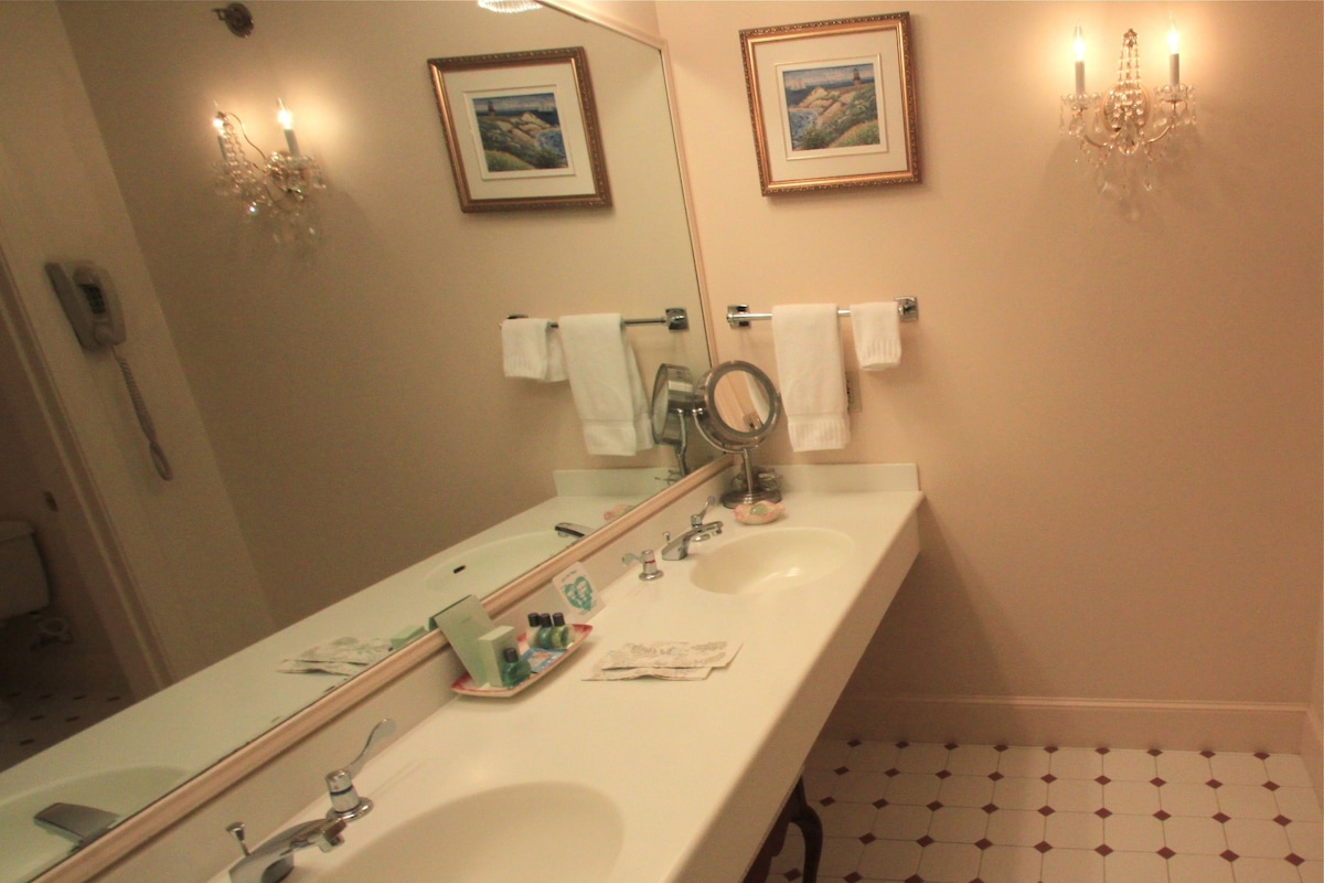 A bathroom with two sinks, a large mirror, a chandelier, and a tiled floor.