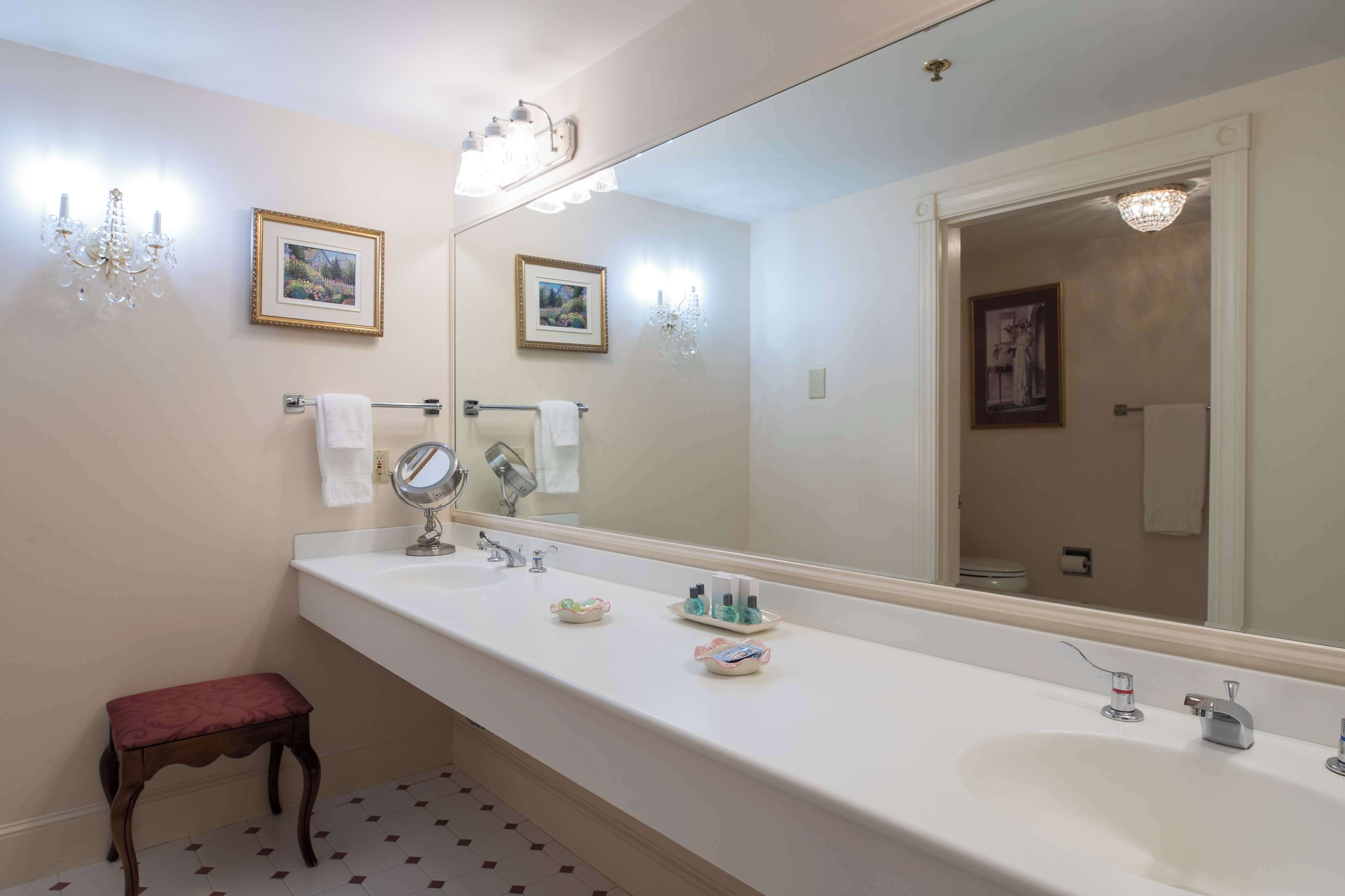 Un baño con un espejo grande, dos lavamanos, un tocador y un taburete pequeño.