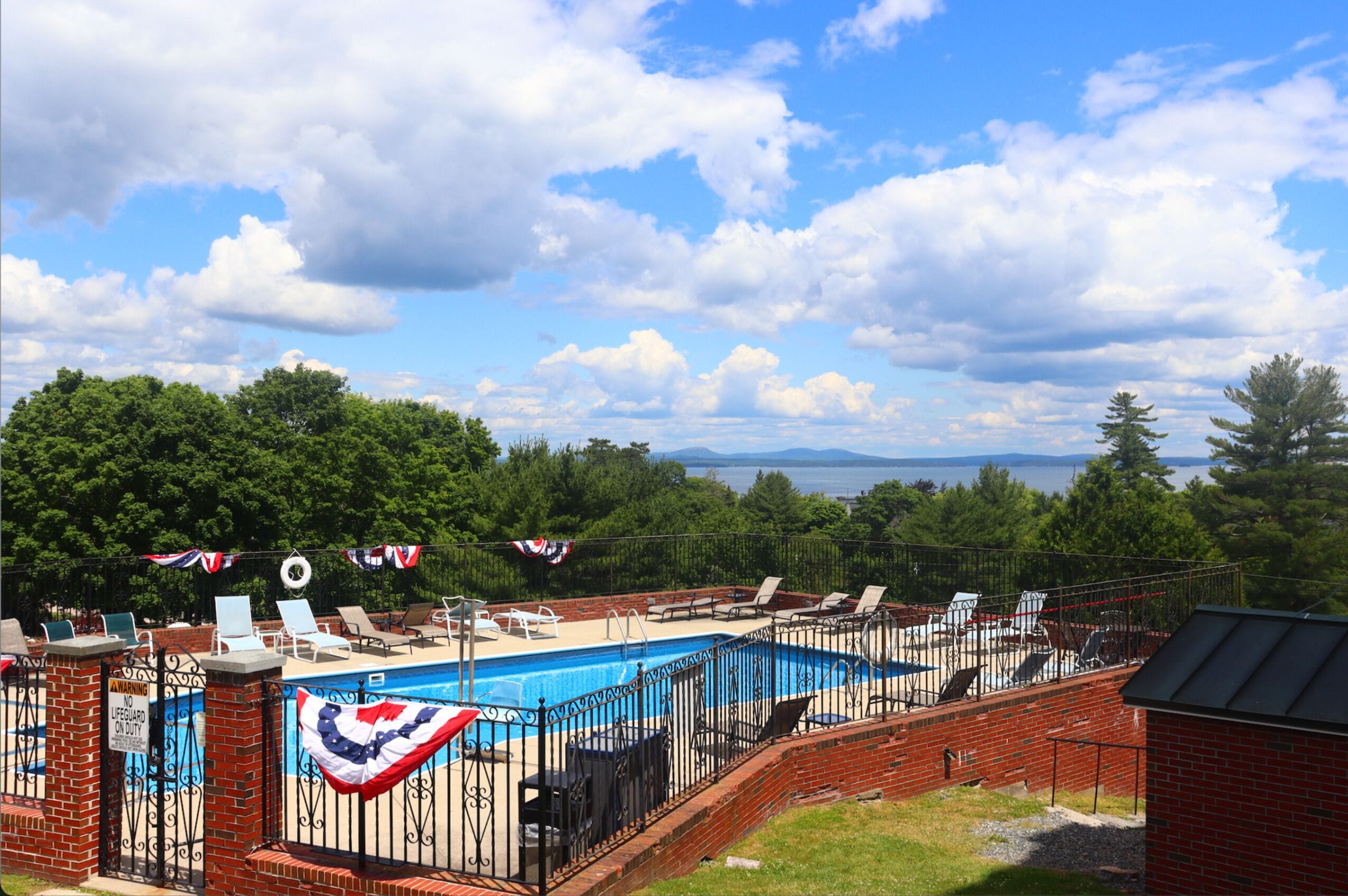 A swimming pool with lounge chairs and a flag decoration, surrounded by a brick wall and trees.