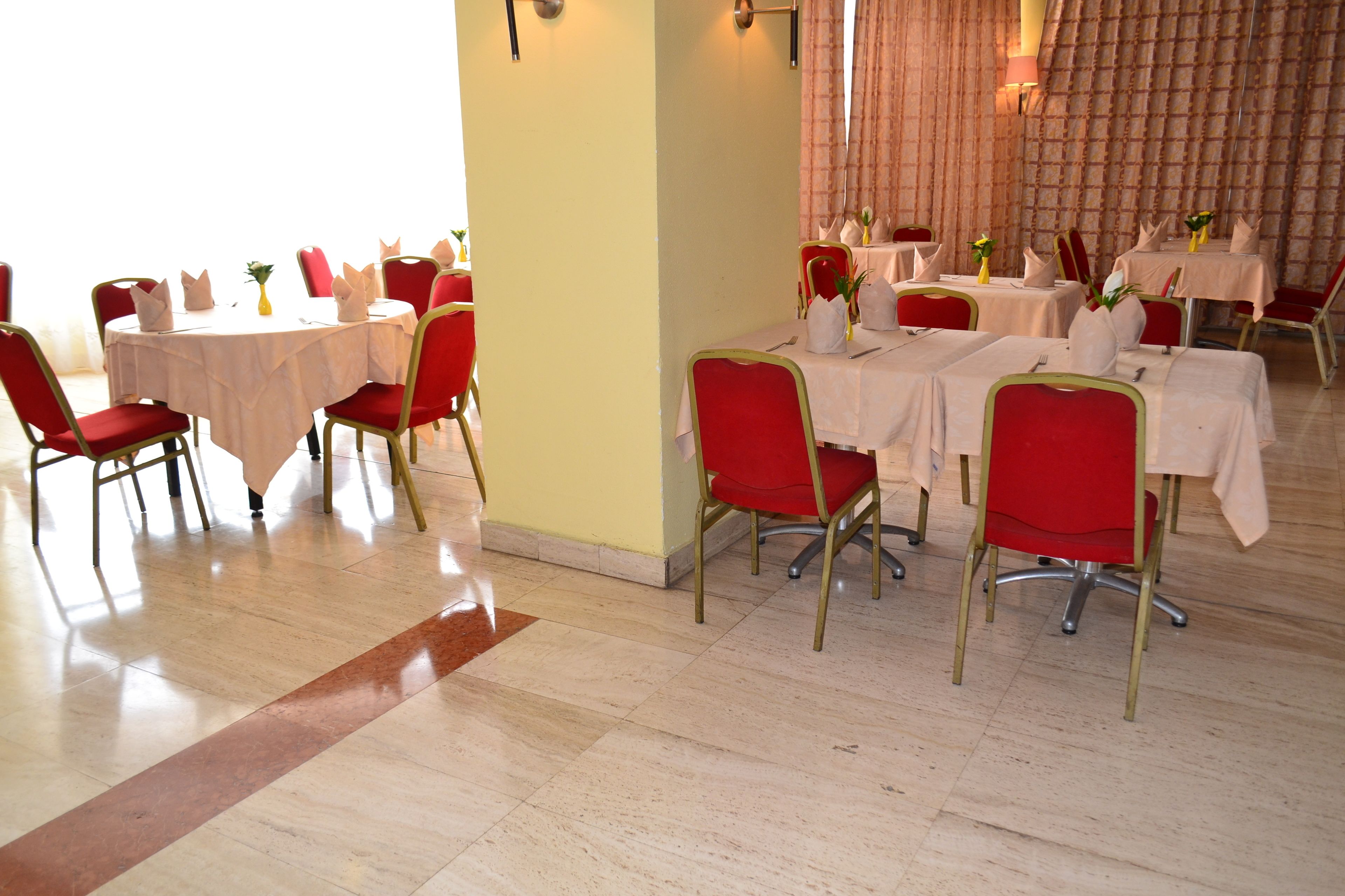 Un comedor con mesas redondas, sillas rojas y manteles blancos.