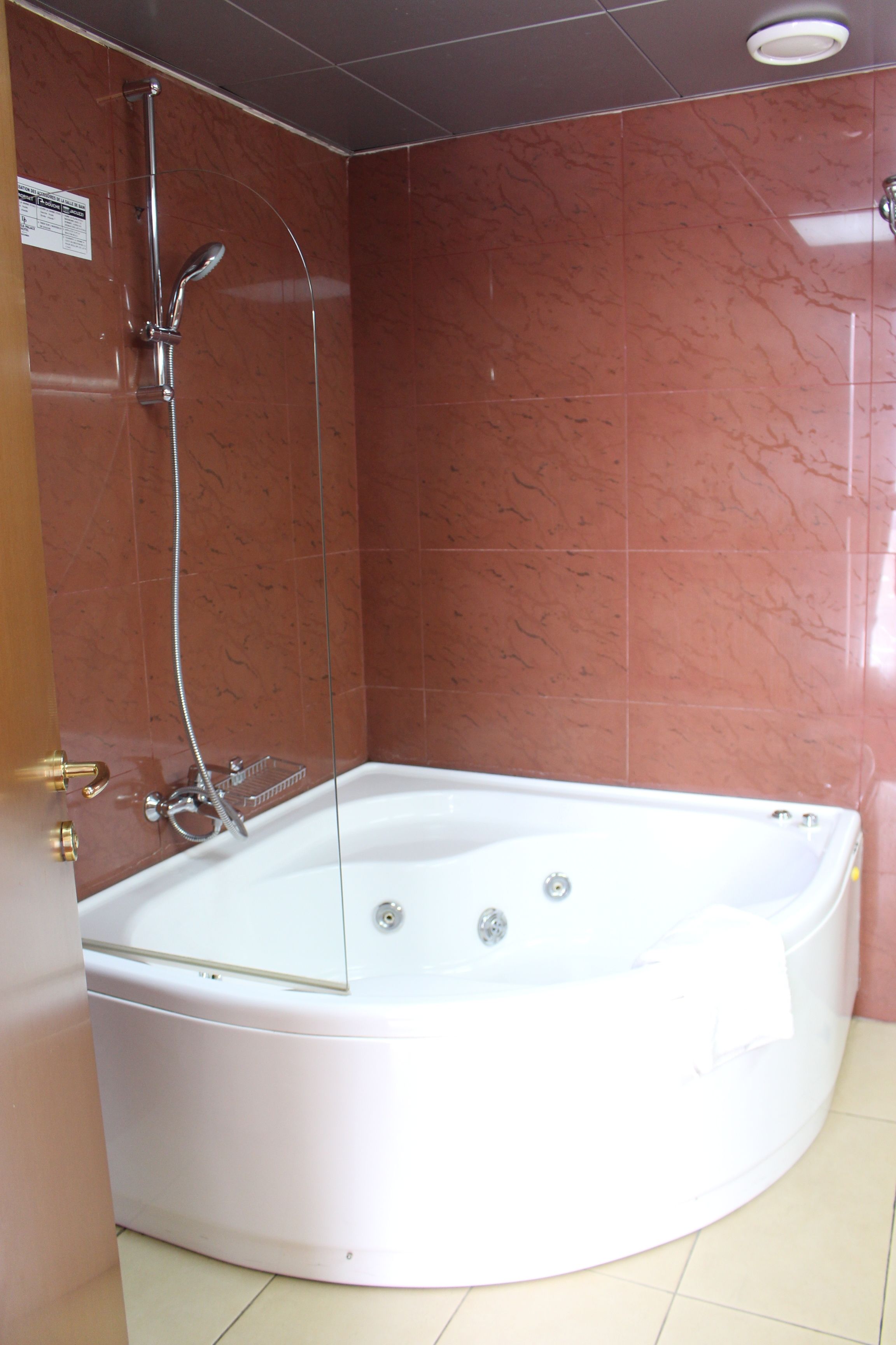 Baño en esquina con bañera blanca, ducha con cerramiento de vidrio y paredes de mármol rojo.