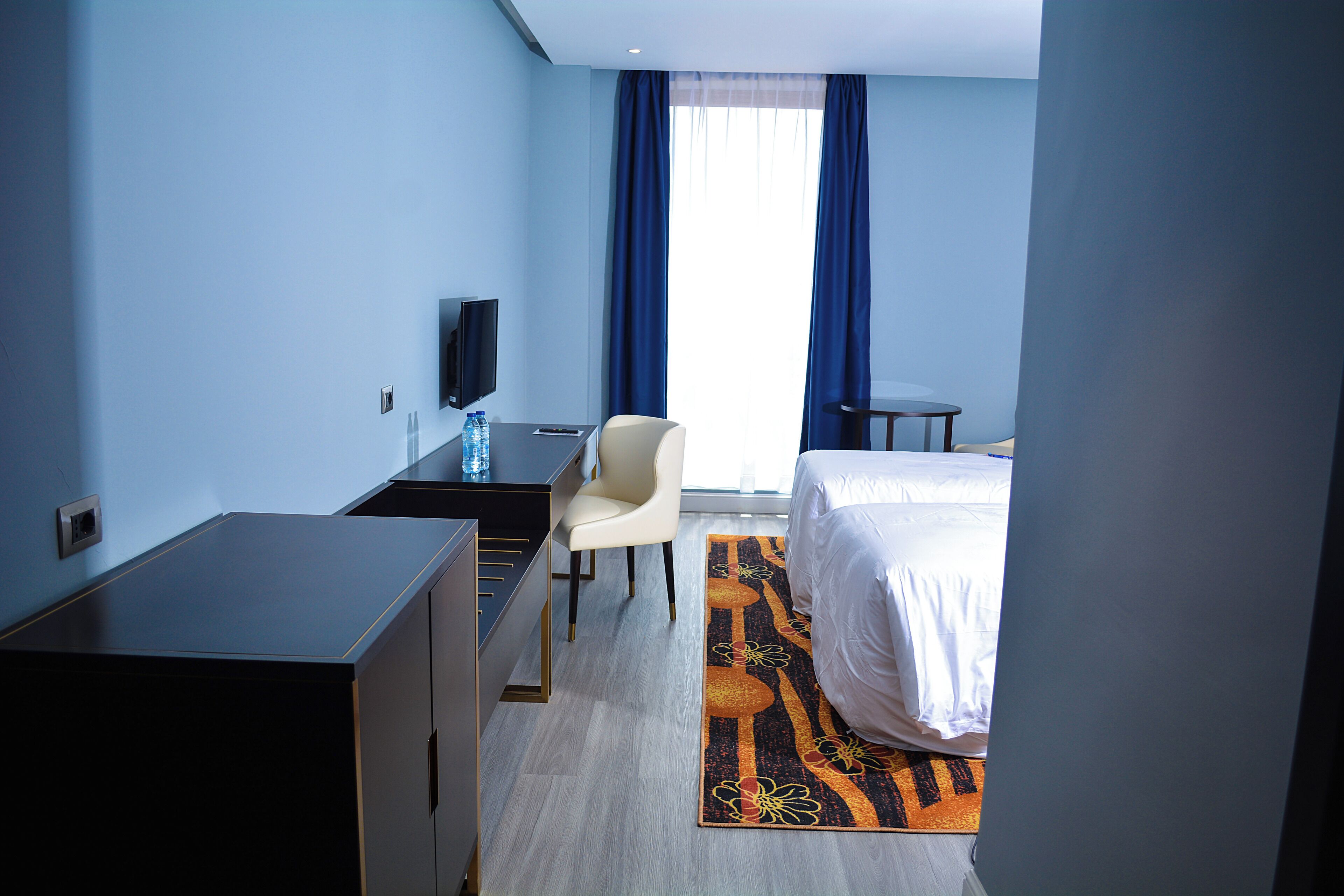 A hotel room with a bed, a desk with a chair, a television, and a window with curtains.
