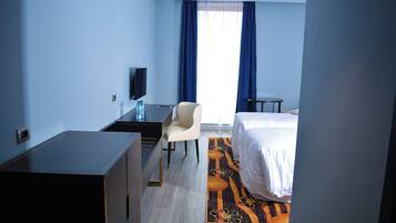 A hotel room with a bed, a desk with a chair, a television, and a window with curtains.