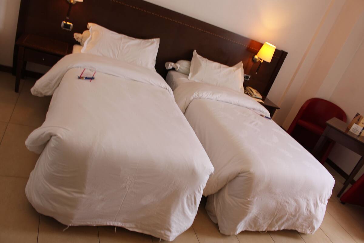 Habitación de hotel con dos camas, una mesita de noche, una lámpara y una silla roja.