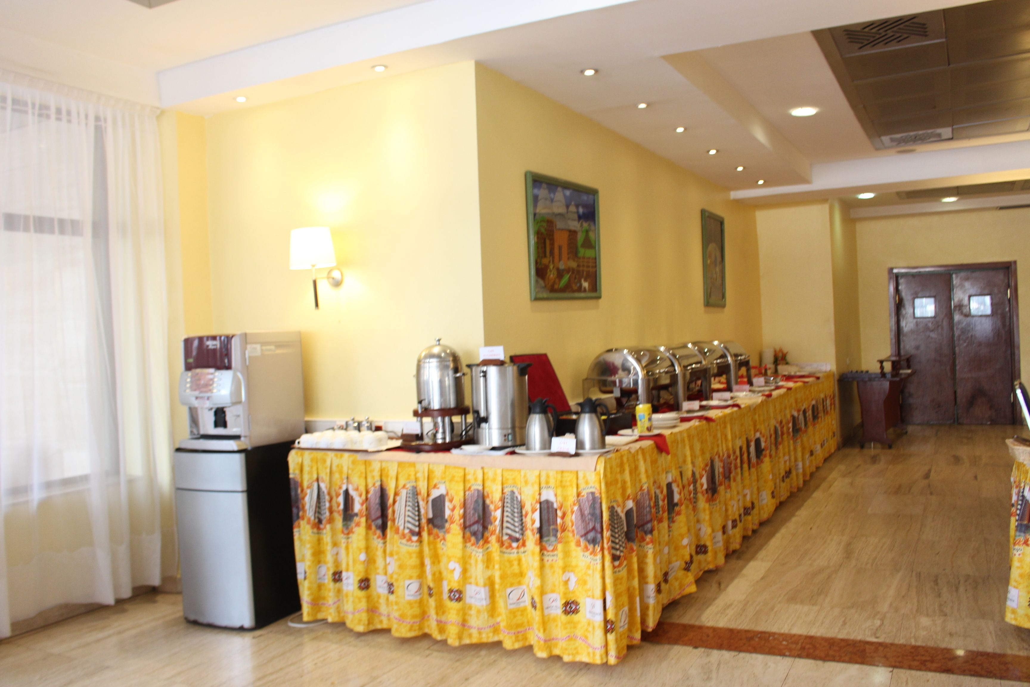 A buffet setup with a coffee machine, multiple serving stations, and a long table covered with a yellow tablecloth.