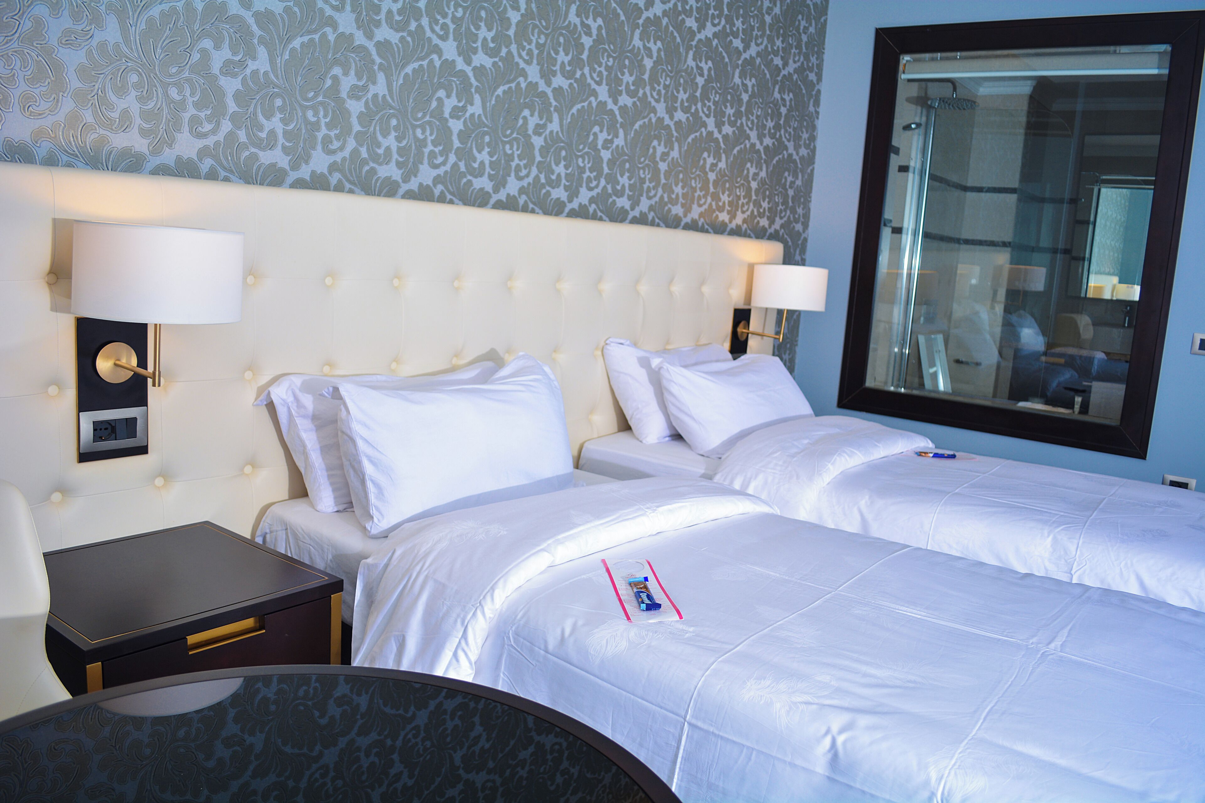 A hotel room with two beds, a nightstand, a table, and a large mirror.