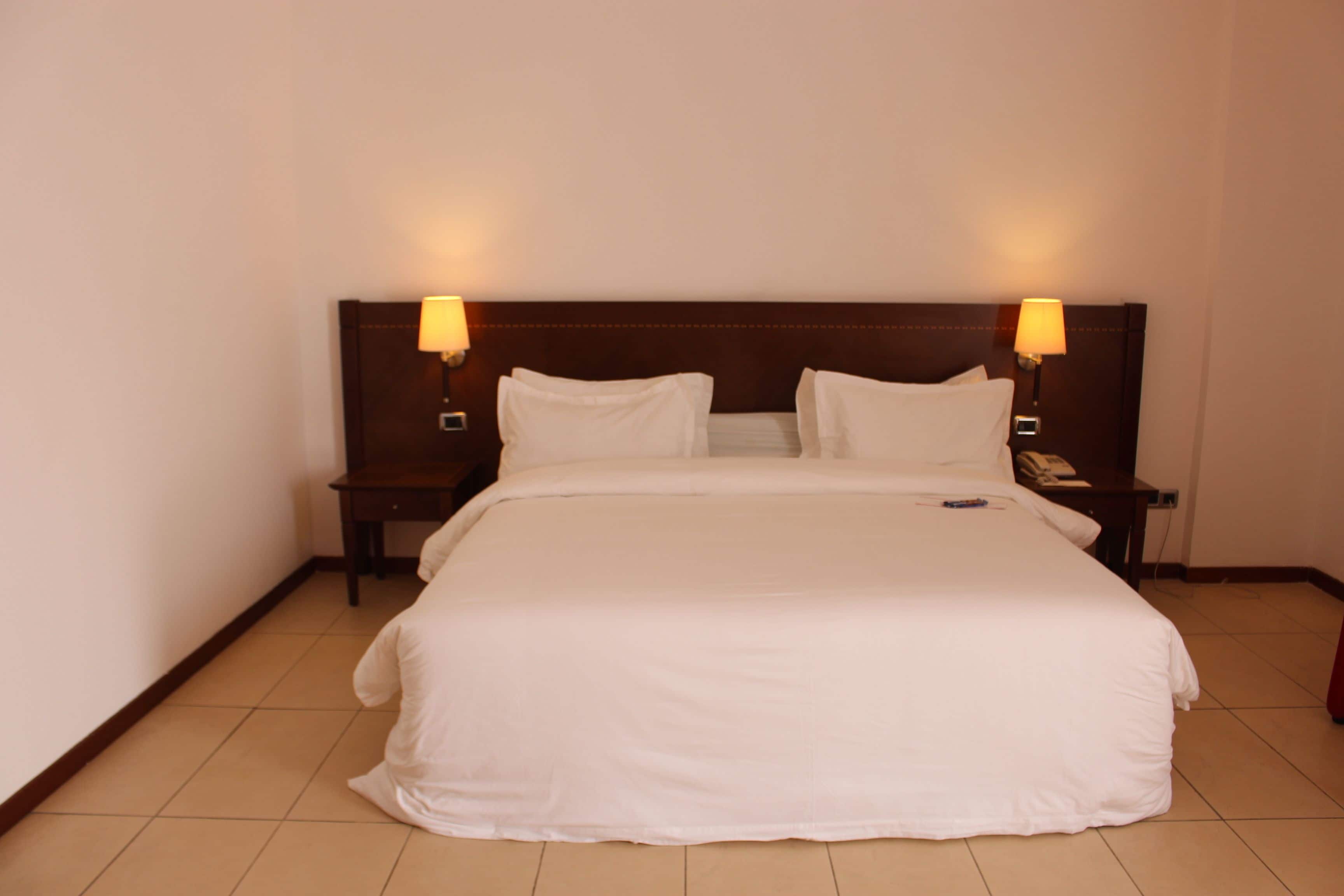 A neatly made bed with white linens, two bedside lamps, and a wooden headboard.