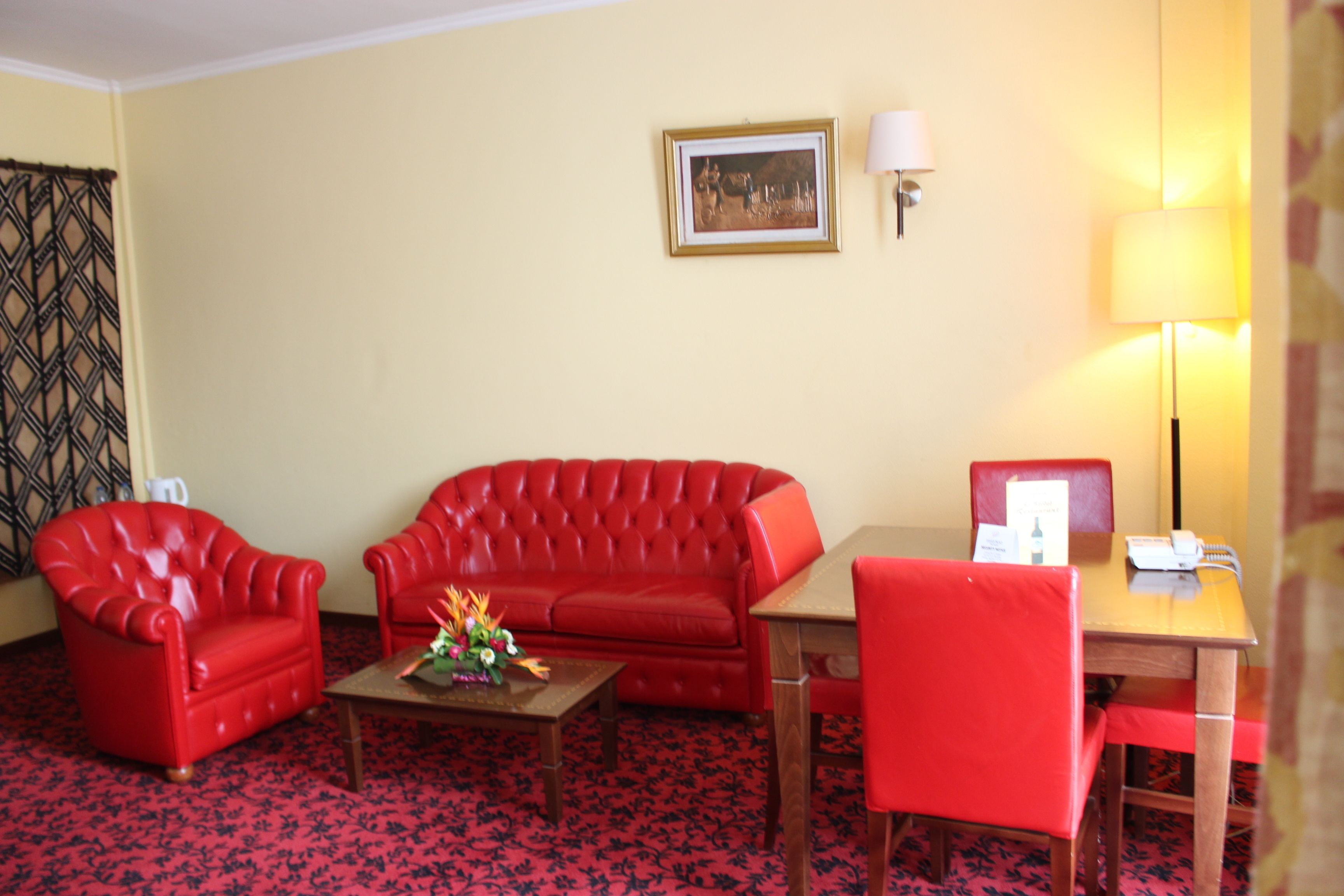 A room with a red sofa, a red armchair, a wooden table, and a lamp.