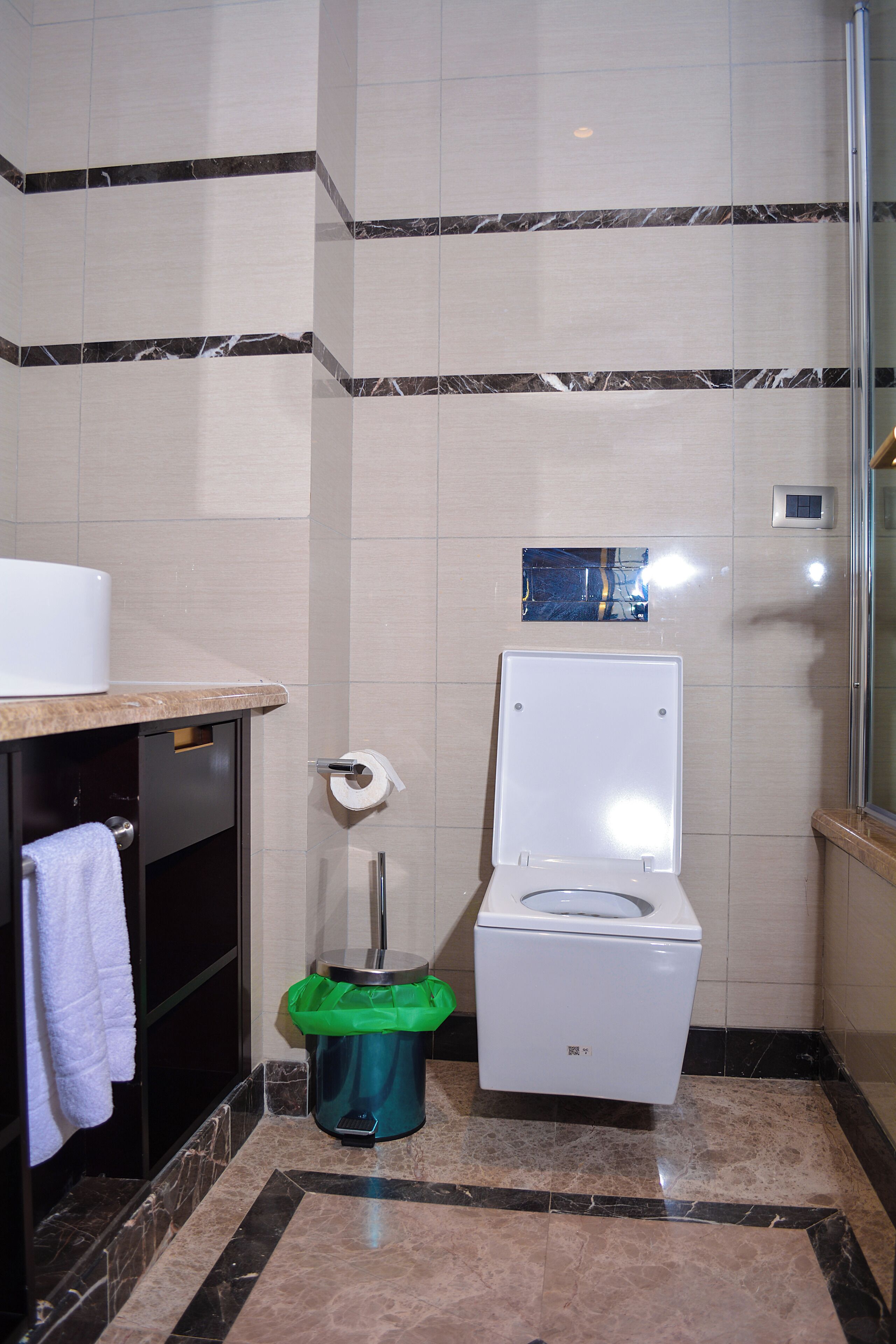 A bathroom with a toilet, a trash bin, a towel rack, and a mirror.