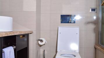A bathroom with a toilet, a trash bin, a towel rack, and a mirror.