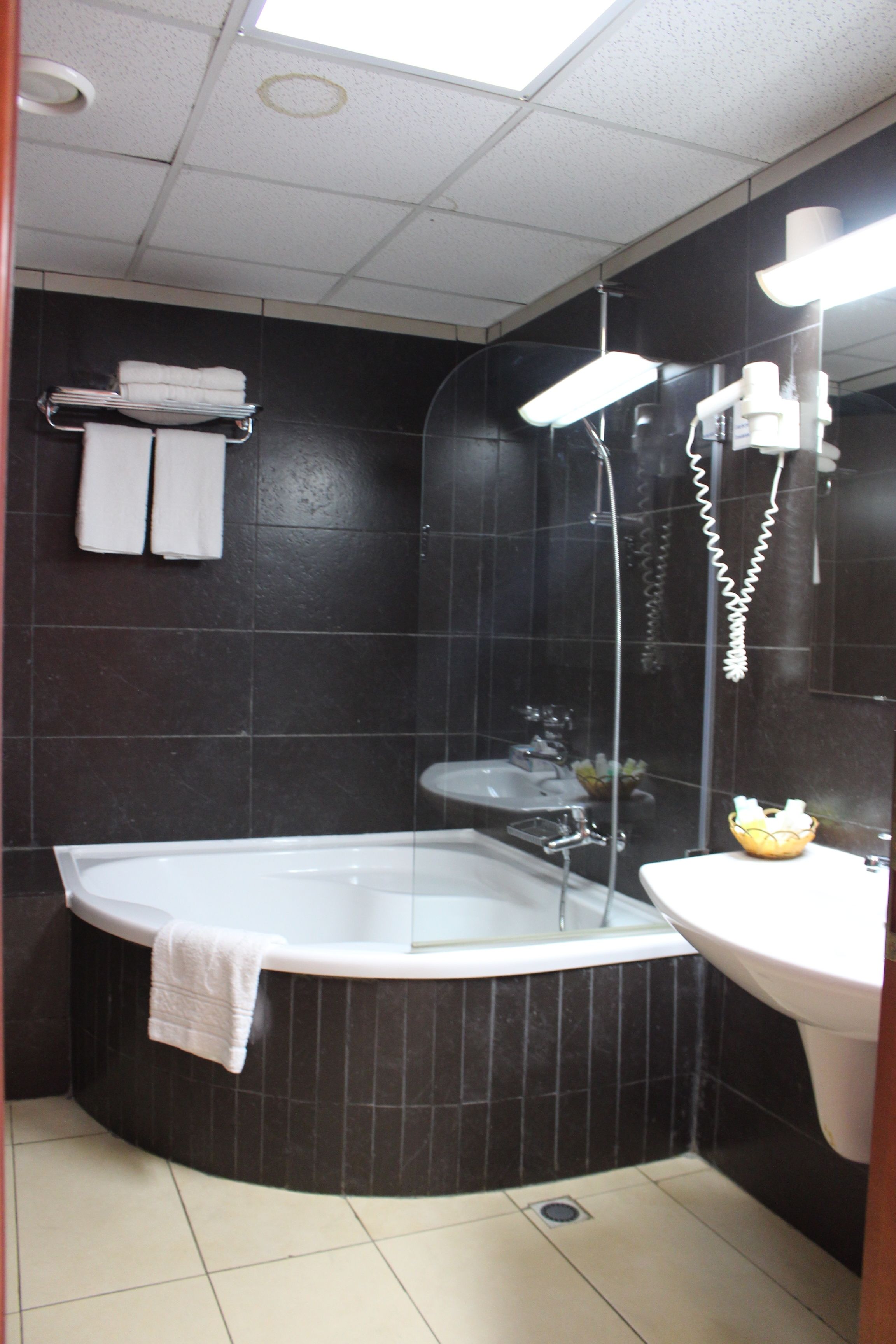 Une salle de bain avec une baignoire, un lavabo et une douche. Des serviettes sont suspendues sur un porte-serviettes et un sèche-cheveux est fixé au mur.