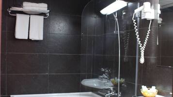 Une salle de bain avec une baignoire, un lavabo et une douche. Des serviettes sont suspendues sur un porte-serviettes et un sèche-cheveux est fixé au mur.