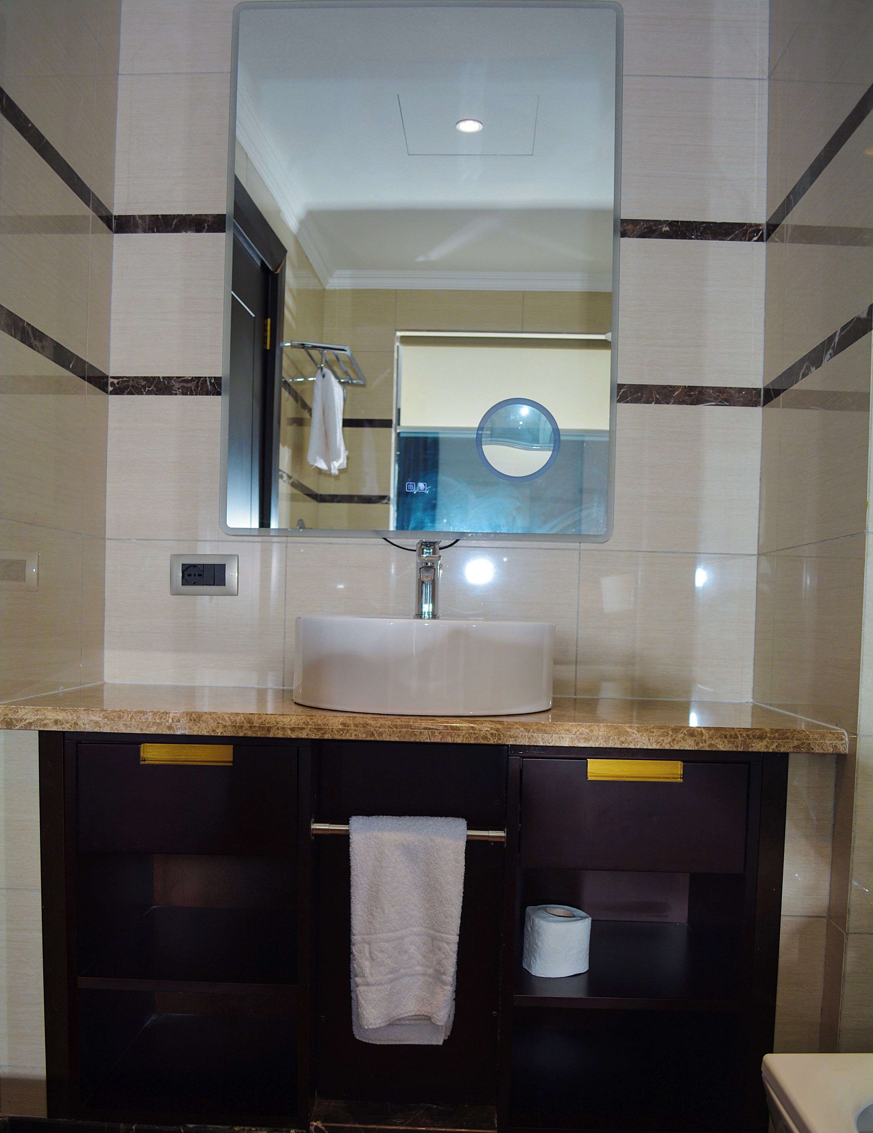 A bathroom with a sink, mirror, towel rack, and toilet paper.