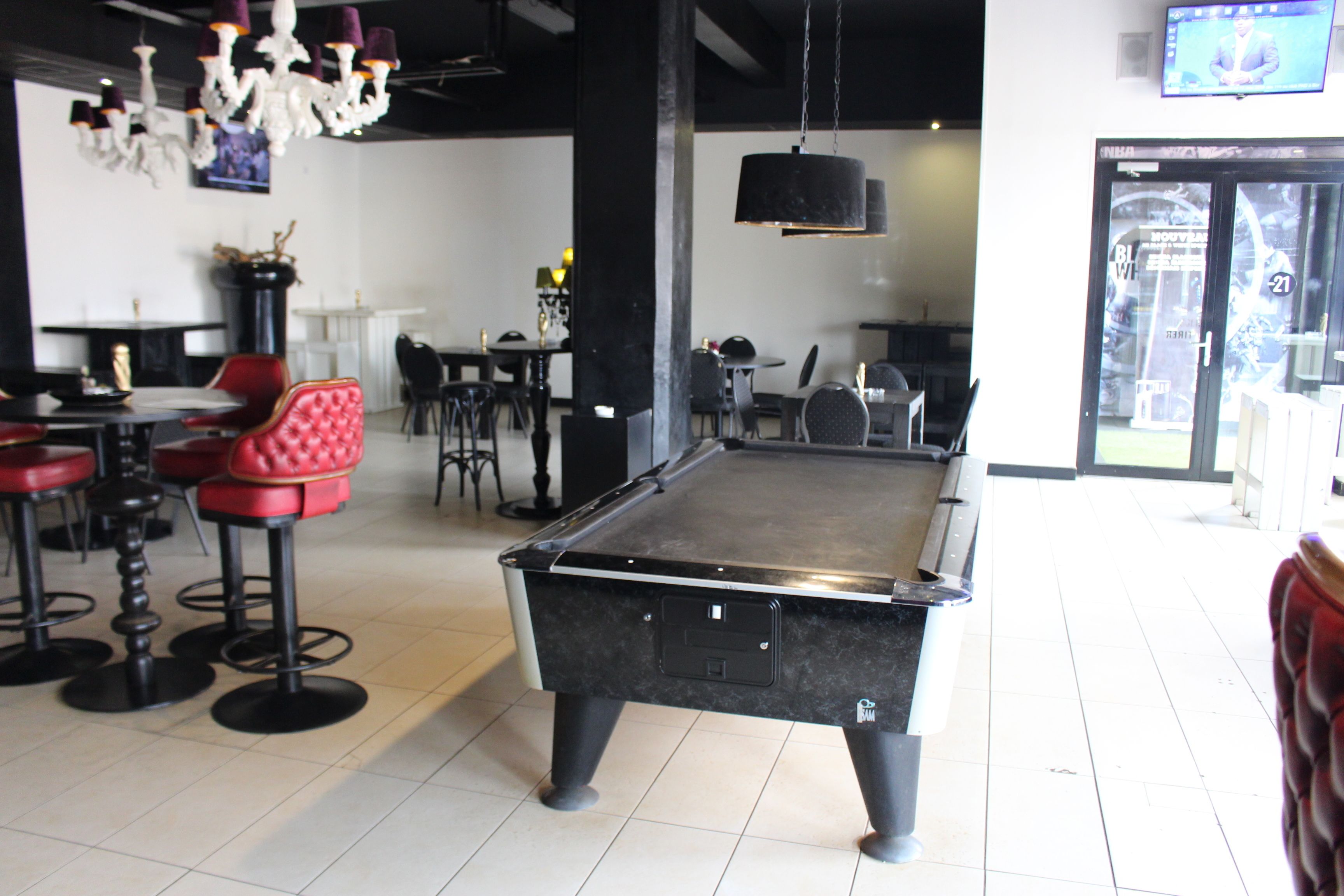 A billiards table in a room with red bar stools, a chandelier, and a television on the wall.