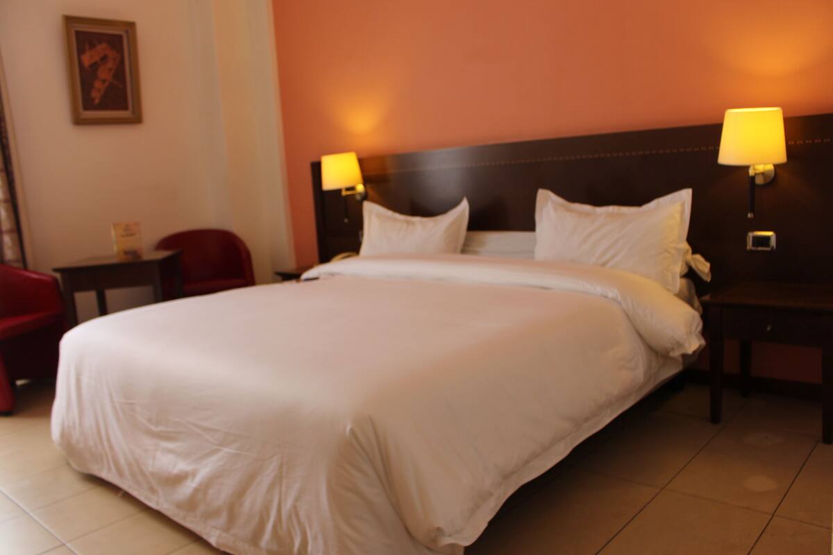 Una habitación de hotel con una cama grande, dos lámparas de noche, una mesita de noche y una silla roja.