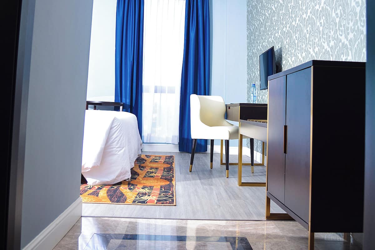 Una habitación de hotel con una cama, un escritorio, una silla, un televisor y un papel tapiz estampado.