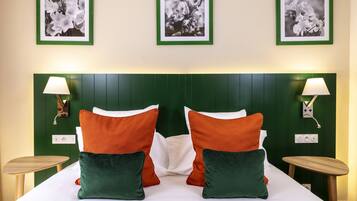 A neatly made bed with white and orange pillows, green headboard, and two bedside tables with lamps.