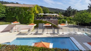 A pool area with lounge chairs and umbrellas, surrounded by greenery and a hillside in the background.