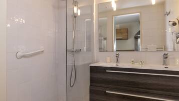 A modern bathroom with a glass shower enclosure, a vanity with a dark wood finish, and a mirror with integrated lighting.