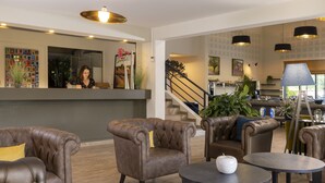 A lobby with leather armchairs, a reception desk, and a staircase leading to upper floors.