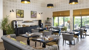 A modern dining area with tables and chairs, a sofa, and a kitchen in the background.