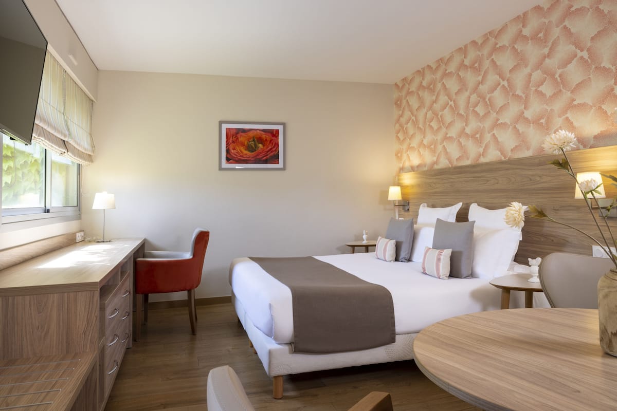A hotel room with a bed, bedside tables, a desk, and a chair.