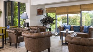 A modern living room with leather sofas, a coffee table, and a lamp. There is a large window with a view of greenery outside.