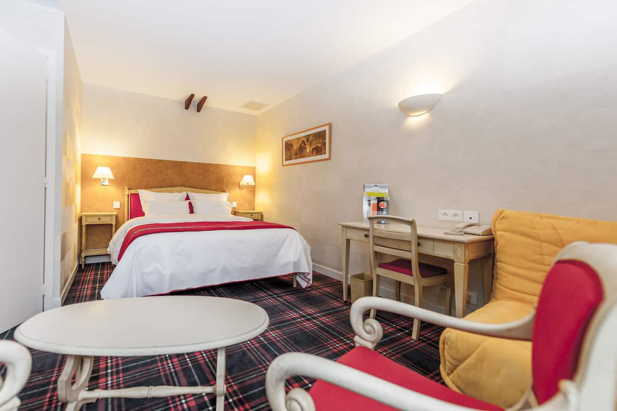 A hotel room with a bed, a desk, a chair, and a small table.