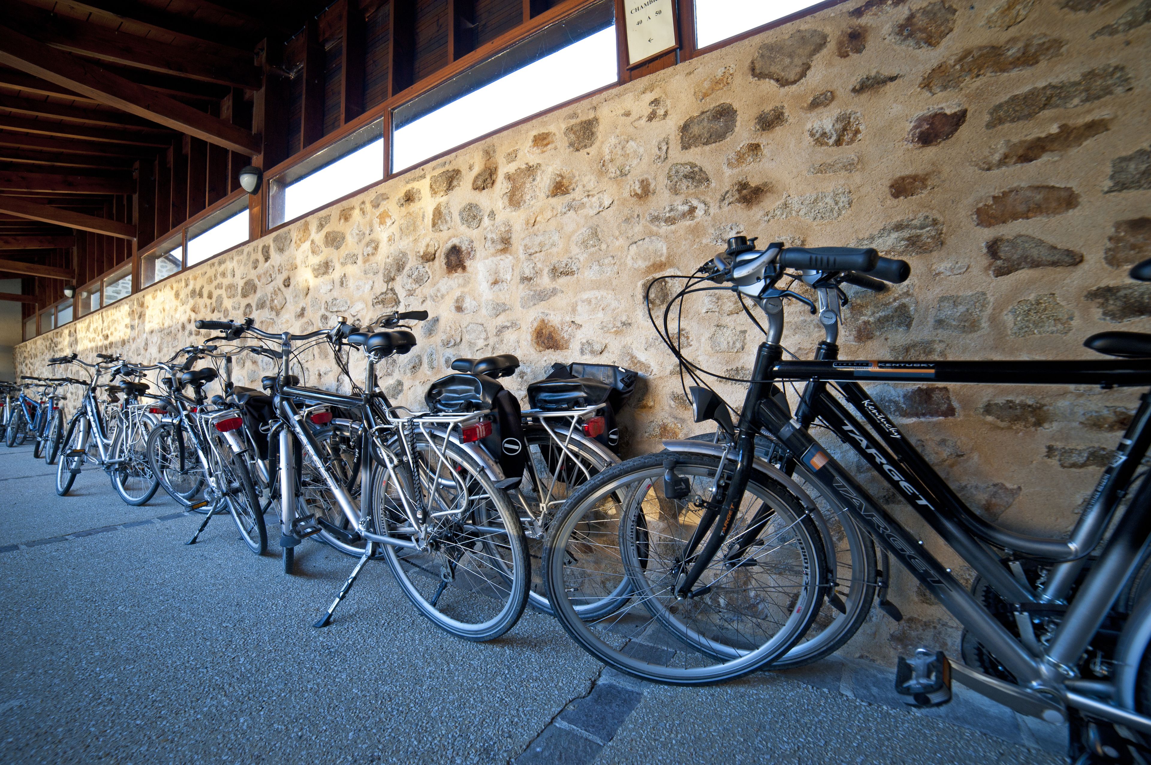 Varias bicicletas están estacionadas junto a un muro de piedra en un espacio cubierto con vigas de madera.