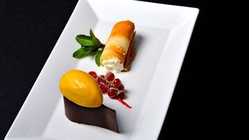 A dessert on a white plate with a chocolate base, a rolled pastry, a yellow fruit, and red berries.