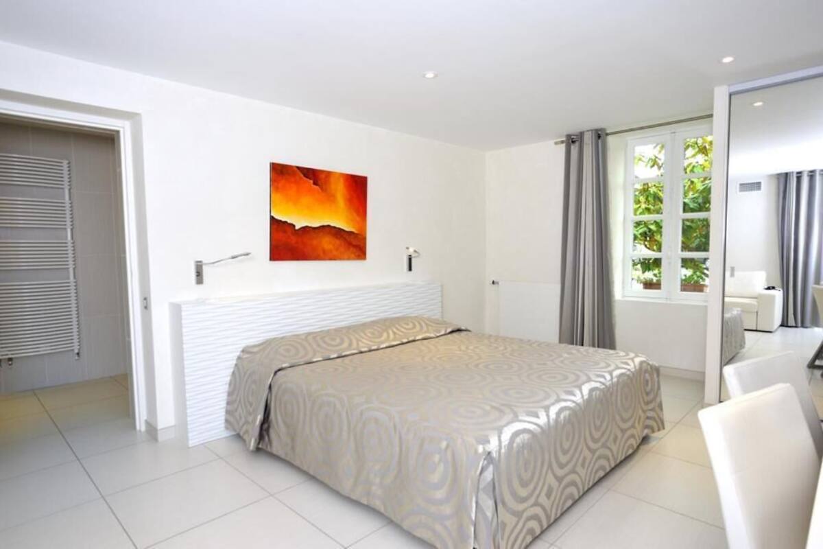A modern bedroom with a bed, a painting, a window with curtains, and a door.