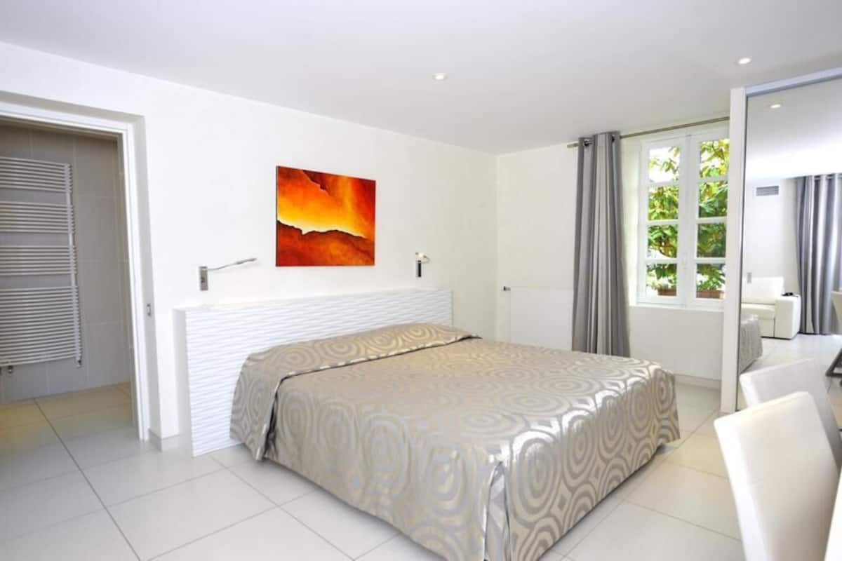 A modern bedroom with a bed, a painting, a window with curtains, and a door.